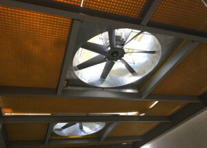 Two large industrial ceiling fans are mounted within a metal framework and FRP cover top grating, viewed from below.