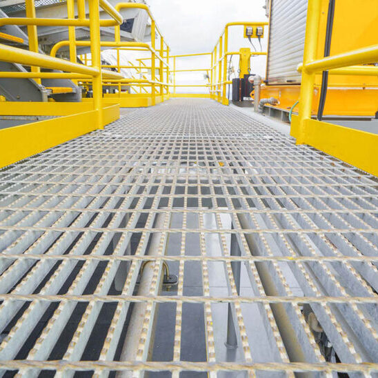 Steel grating walkway with yellow handrails in industrial setting.