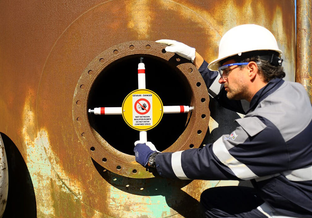 Manhole entry confined space barrier with worker in industrial environment.