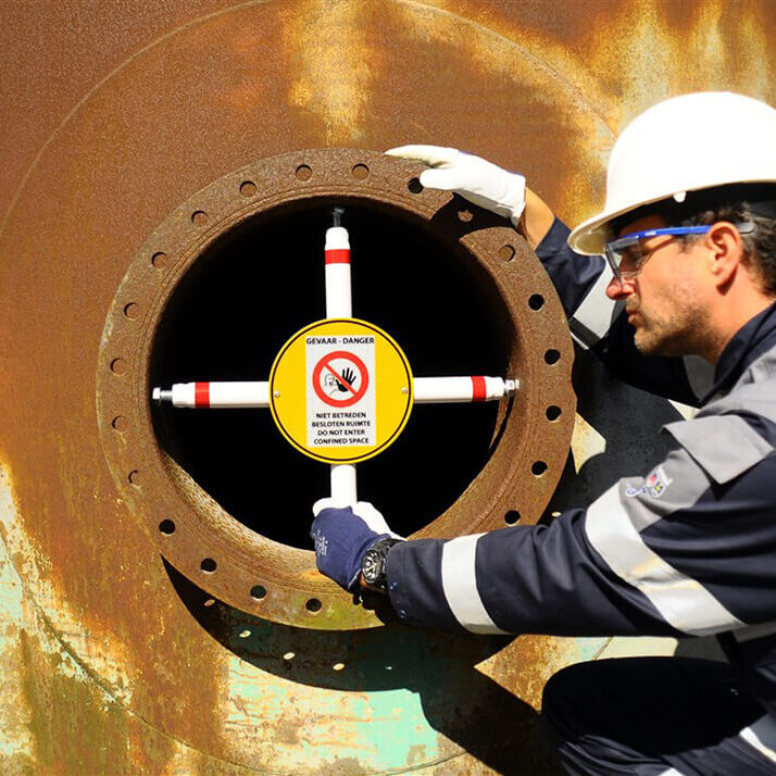 Manhole entry confined space barrier with worker in industrial environment.